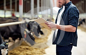 Farmer with clipboard and cows in cowshed on farm photo