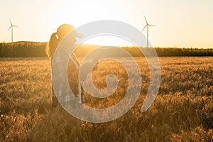 Farmer with digital tablet on the field. Wind turbines on a horizon. Sustainable farming and agriculture digitalization