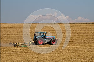 a blue tractor on a harvested grain field