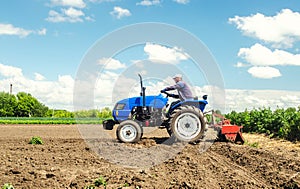 Farmer drives a tractor with a milling machine. Loosens, grind and mix soil on plantation field. Field preparation for new crop