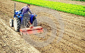 Farmer drives a tractor with a milling machine. Loosens, grind and mix soil on plantation field. Field preparation for new crop