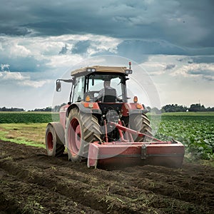 Farmer Driving Tractor Working Soil in Agricultural Field Under Cloudy Sky