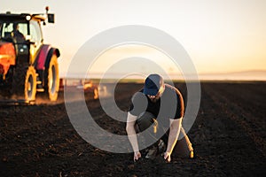 Farmer examing dirt while tractor is plowing field