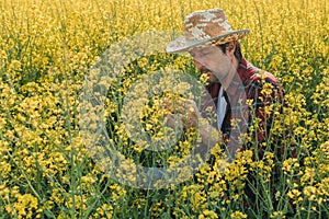 Farmer examining blooming rapeseed plant in cultivated field