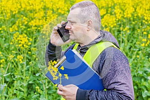 Farmer with folder and cell phone near yellow field