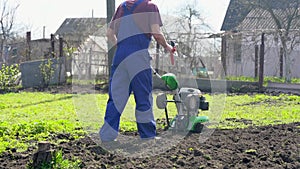 A farmer in the garden tills the land with a motorized cultivator or power tiller, preparing the soil for planting crops