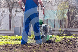 A farmer in the garden tills the land with a motorized cultivator or power tiller, preparing the soil for planting crops