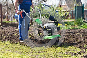 A farmer in the garden tills the land with a motorized cultivator or power tiller, preparing the soil for planting crops