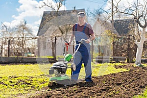 A farmer in the garden tills the land with a motorized cultivator or power tiller, preparing the soil for planting crops