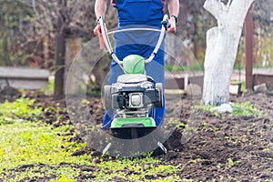 A farmer in the garden tills the land with a motorized cultivator or power tiller, preparing the soil for planting crops