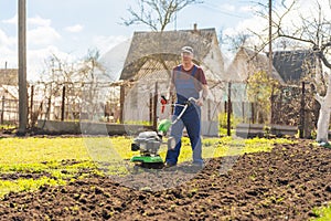 A farmer in the garden tills the land with a motorized cultivator or power tiller, preparing the soil for planting crops