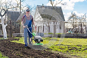 A farmer in the garden tills the land with a motorized cultivator or power tiller, preparing the soil for planting crops