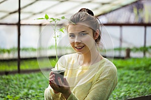 Farmer girl holding green seedlings in sunny greenhouse