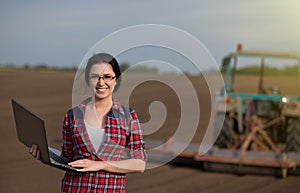 Farmer girl with laptop in field with tractor