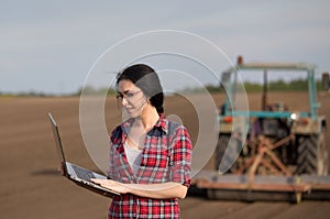 Farmer girl with laptop in field with tractor