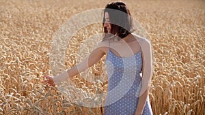 Farmer girl walking on summer wheat field, her hands touching ripe wheat ears. Harvest concept