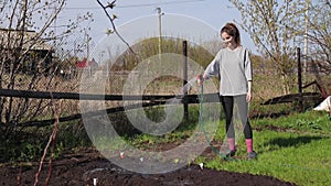 Farmer girl watering the garden beds with a garden sprayer in the village