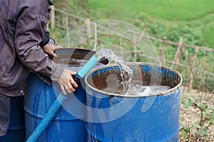 farmer hand hold pipe of water to put into blue buckets in garden. Concept, Solve problems lacking of water in agriculture