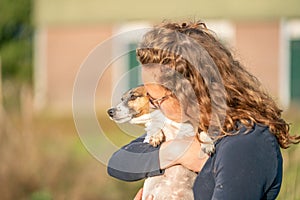 Farmer and her love for pets. Jack Russell Terrier dog lies in the woman`s arms. stable in background