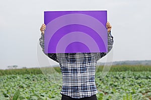 Farmer hold blank violet paper poster at garden background