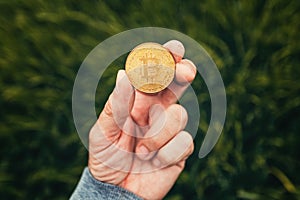 Farmer holding Bitcoin cryptocurrency coin in green barley field