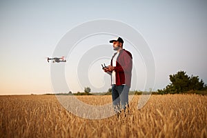 Farmer holds remote controller with his hands while quadcopter is flying on background. Drone hovers behind the
