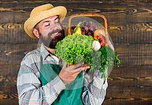 Farmer with homegrown vegetables in basket. Man bearded farmer presenting eco vegetables wooden background. Fresh