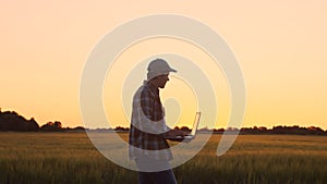 Farmer with a laptop computer in front of a sunset agricultural landscape. Man in a countryside field. Country life