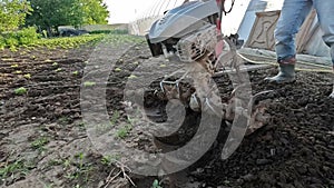 A farmer man plows the land with a cultivator machinery for soil cultivation in the garden, using tiller block