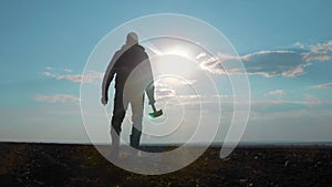 Farmer man silhouette red neck holding a shovel in his hand walking across the field a pile of dirt soil. Eco smart