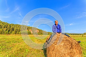 Farmer man sitting on a straw bale in a field.