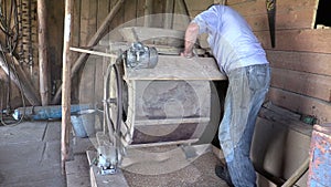 Farmer man spin handle of sifting machine and sift grain in mill