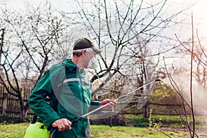 Farmer man spraying tree with manual pesticide sprayer against insects in spring garden. Agriculture and gardening