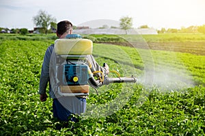 A farmer with a mist fogger sprayer sprays fungicide and pesticide on potato bushes. Effective crop protection, environmental