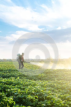 A farmer with a mist sprayer blower processes the potato plantation from pests and fungus infection. Fumigator fogger. Use