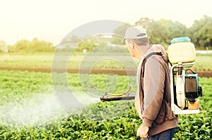 A farmer with a mist sprayer spray treats the potato plantation from pests and fungus infection. Agriculture and agribusiness.