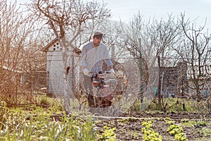 Farmer performing garden soil tillage with old poor cultivator tiller agricultural machine