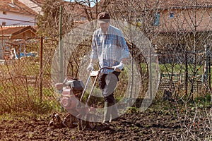 Farmer performing garden soil tillage with old poor cultivator tiller agricultural machine