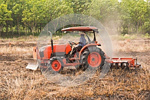 Farmer plowing stubble field with orange tractor