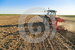 Farmer plowing stubble field with red tractor