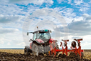 Farmer plowing stubble field with red tractor.