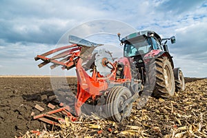 Farmer plowing stubble field with red tractor.