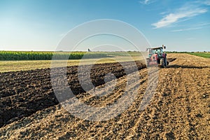 Farmer plowing stubble field with red tractor.