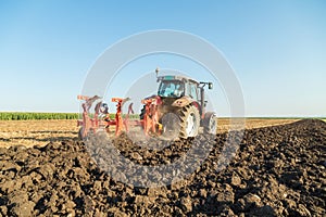 Farmer plowing stubble field with red tractor.