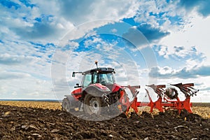 Farmer plowing stubble field with red tractor.