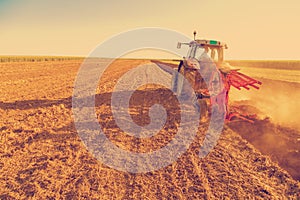 Farmer plowing stubble field with red tractor