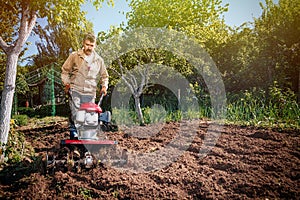 Farmer plows the land with a cultivator, preparing it for planting vegetables, on a sunny day garden