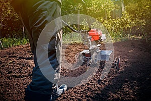 Farmer plows the land with a cultivator, preparing it for planting vegetables, on a sunny day garden