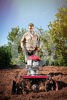 Farmer plows the land with a cultivator, preparing it for planting vegetables, on a sunny day garden