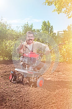 Farmer plows the land with a cultivator, preparing it for planting vegetables, on a sunny day garden